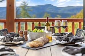 A wooden table set with a bowl of salad, a bottle of wine, two wine glasses, and a loaf of bread on a balcony with a mountain view. - ๐ฎ Arcade & Theater + ๐โโ๏ธ Pool & Hot Tub, ๐ Sleeps 14, ๐ข Near Dollywood (Pigeon Forge)