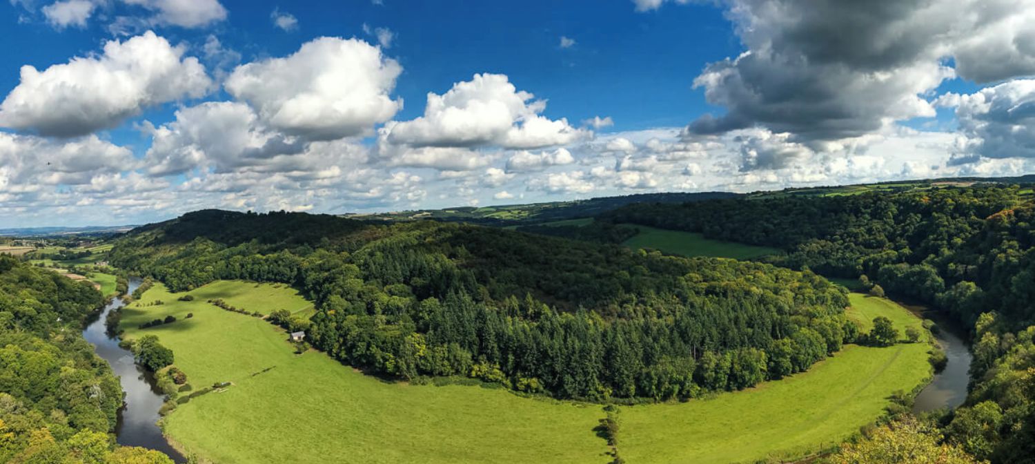 Eine malerische Landschaft mit einem Fluss, der durch ein Tal schlängelt, umgeben von üppiger Vegetation und sanften Hügeln.