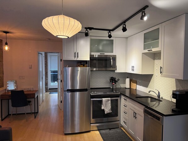 A modern kitchen with stainless steel appliances, white cabinetry, and a unique hexagonal tile backsplash. - Trendy condo in downtown core. (Victoria)