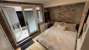 Een slaapkamer met een groot bed, een bakstenen muur en een schuifglazen deur naar een balkon.