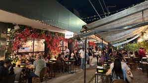 An outdoor dining area with tables and chairs, a covered section with a 'GRAZIE' sign, and a brick wall in the background.