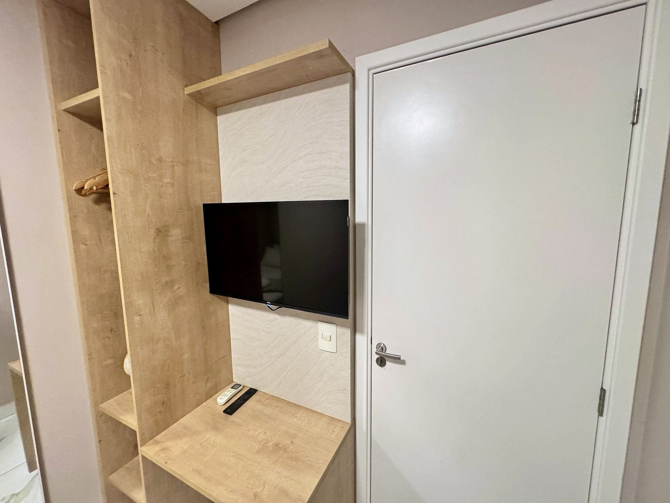 A room with a built-in TV on a wall, a wooden shelf, and a door.