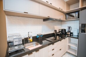 A modern kitchen with white cabinets, a black countertop, and various appliances including a microwave and coffee maker. - Oásis Porto de Galinhas - Flat na Praia (Ipojuca)