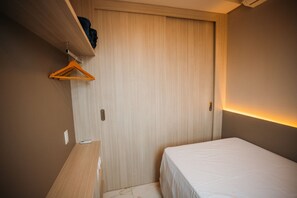 Un dormitorio pequeño y ordenado con una cama individual, un escritorio de madera y un armario.