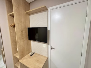 Una habitación con televisión empotrada en la pared, un estante de madera y una puerta.
