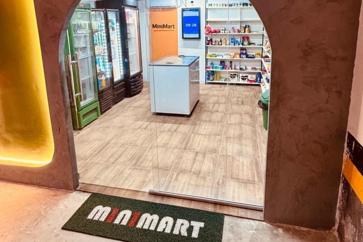An interior view of a MiniMart store with a clear entrance, shelves stocked with products, and a digital display.