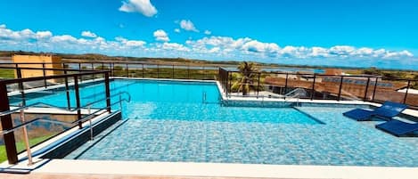 Una piscina rectangular con agua azul cristalina, rodeada por un muelle de madera y barandales de metal.