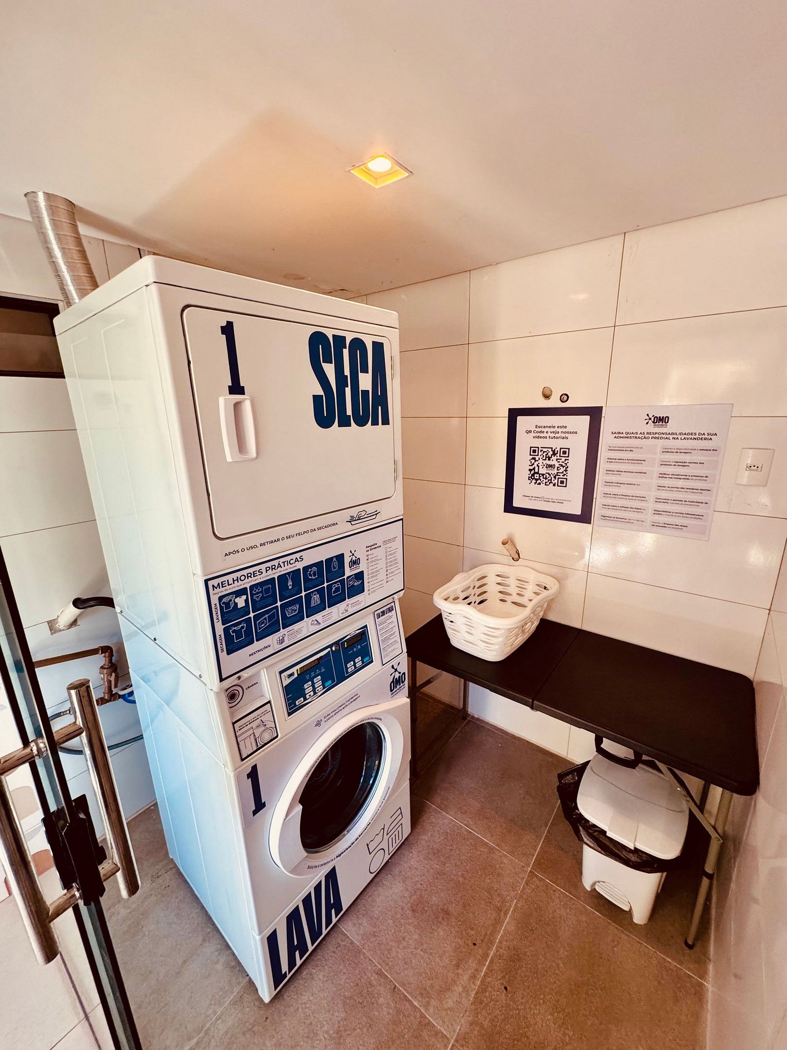 Un cuarto de lavandería con una lavadora SEGA, un código QR para tutoriales y una mesa con una cesta.