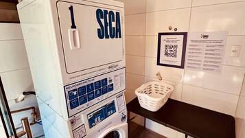 Un cuarto de lavandería con una lavadora SEGA, un código QR para tutoriales y una mesa con una cesta.