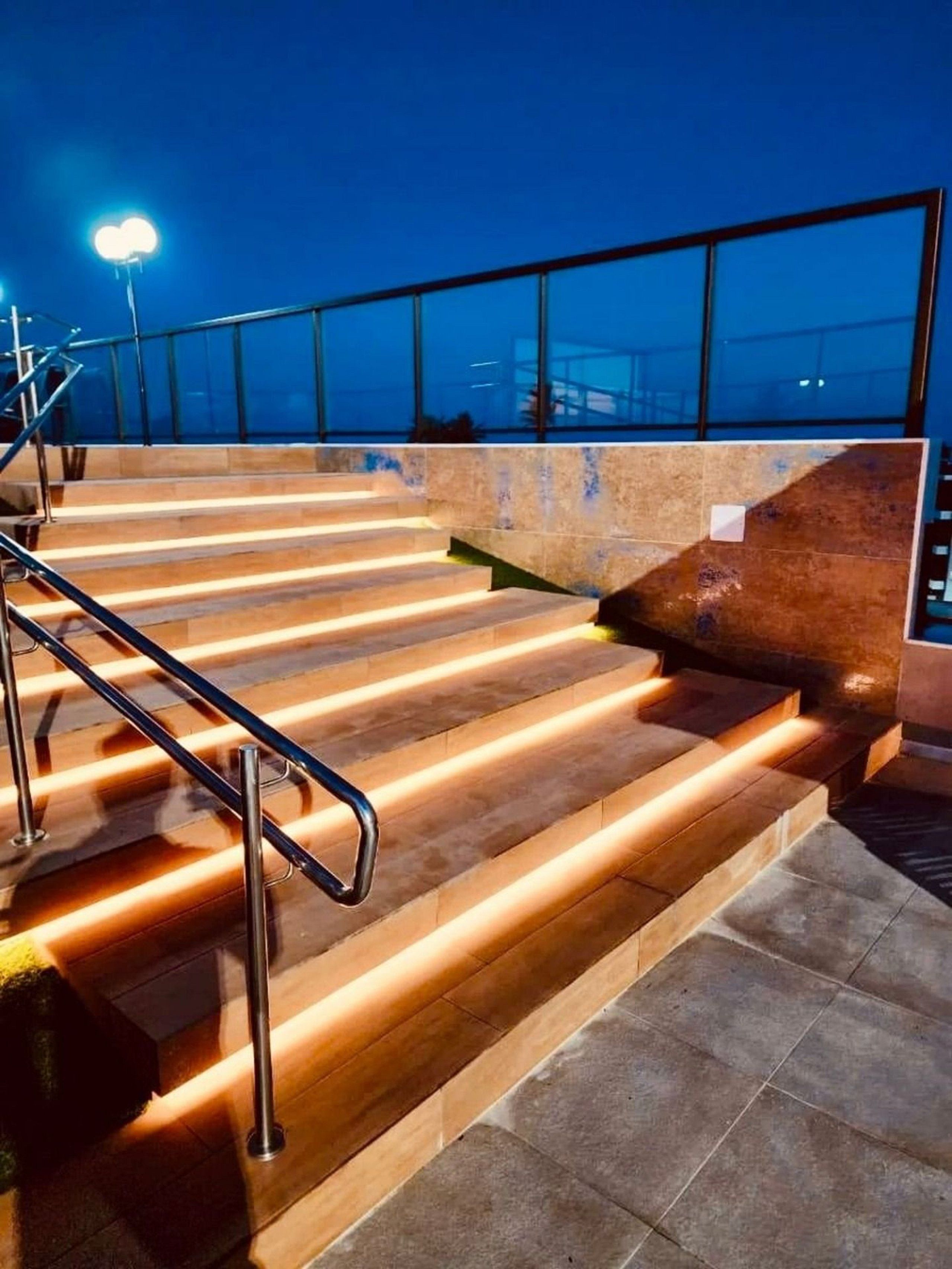 Un conjunto de escalones exteriores con barandillas metálicas que conducen a un nivel superior con una barrera de cristal.