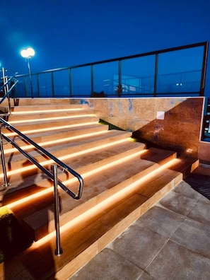 Un conjunto de escalones exteriores con barandillas metálicas que conducen a un nivel superior con una barrera de cristal.