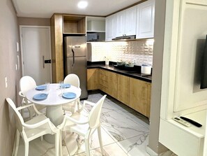 A compact kitchen with white cabinets, a built-in microwave, and a stainless steel refrigerator. - Oásis Porto de Galinhas - Flat na Praia (Ipojuca)