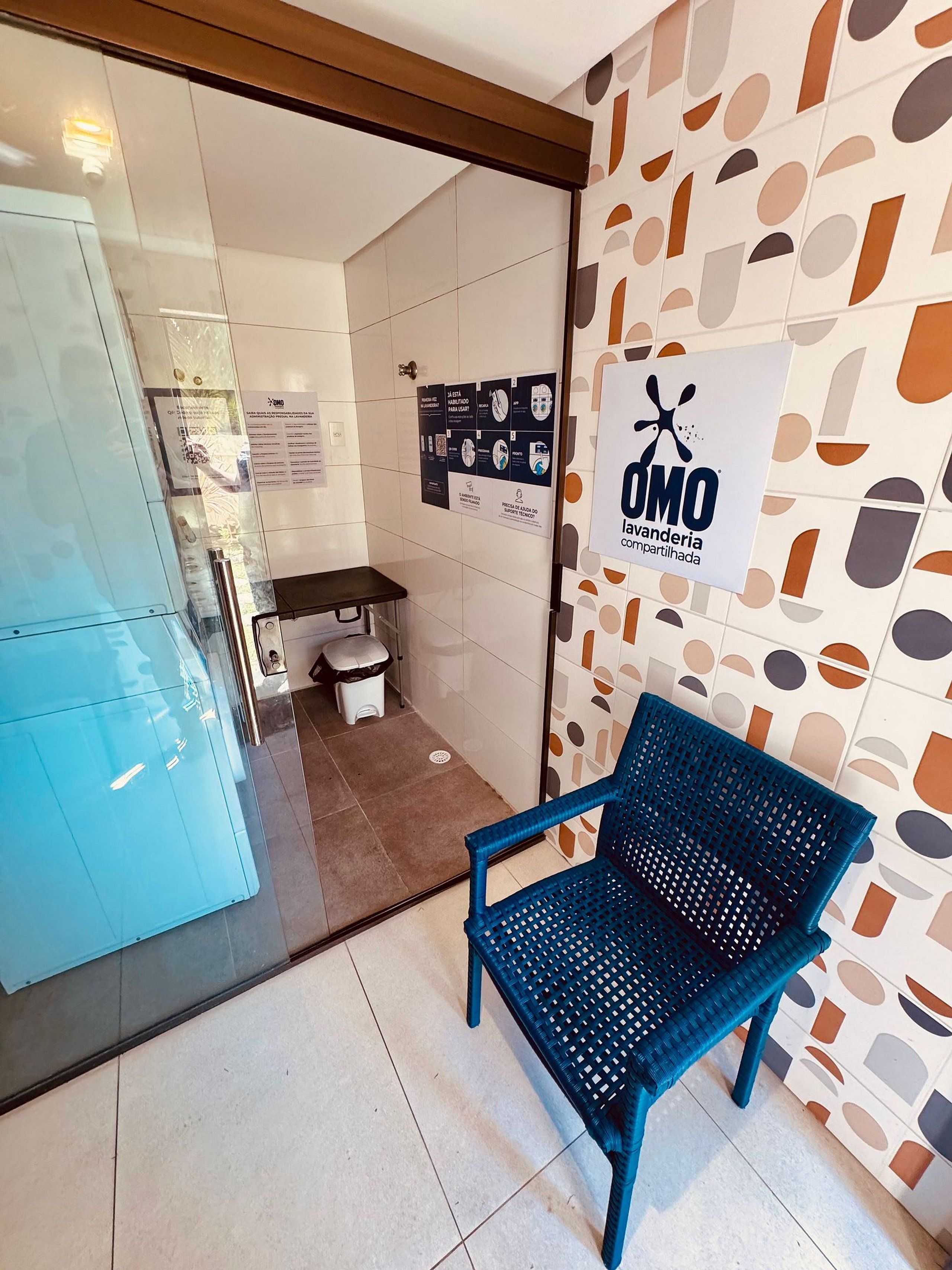 Un área de espera con una silla azul, un panel de vidrio y una pared con carteles informativos.