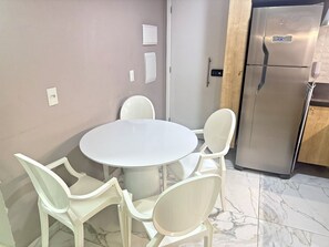 A modern kitchen with a round table and four chairs, a stainless steel refrigerator, and marble flooring. - Oásis Porto de Galinhas - Flat na Praia (Ipojuca)