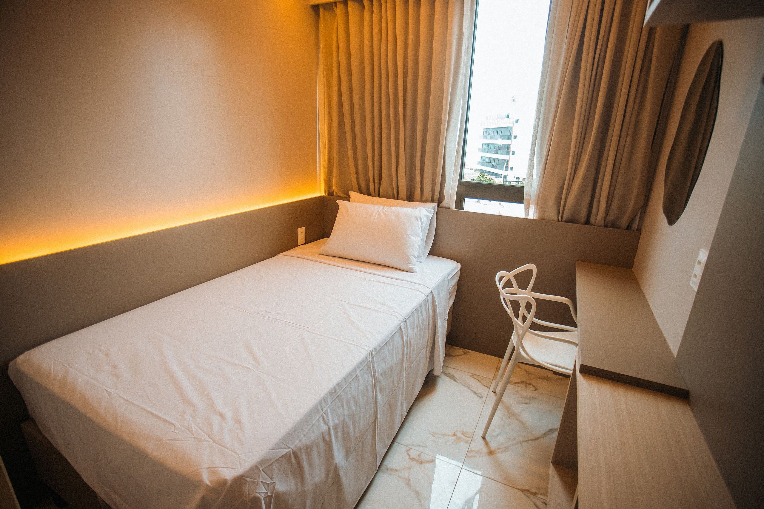 Een compacte, netjes ingerichte hotelkamer met een enkel bed, een stoel en een raam met gordijnen.
