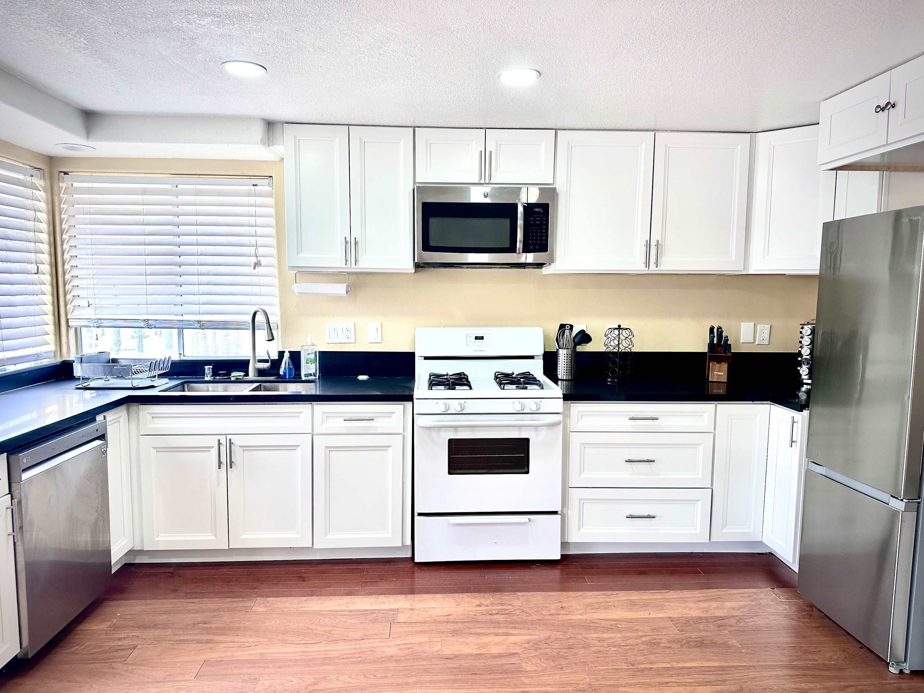 A modern kitchen with white cabinets, stainless steel appliances, and a black countertop.