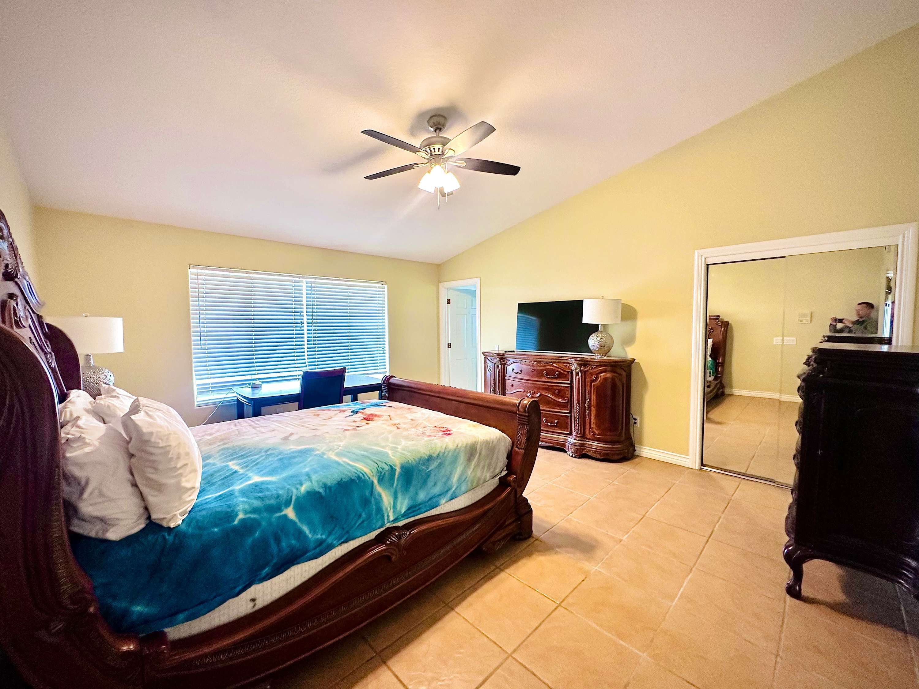 A bedroom with a bed, a ceiling fan, a dresser, a TV, and a mirror.