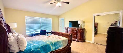 A bedroom with a bed, a ceiling fan, a dresser, a TV, and a mirror.