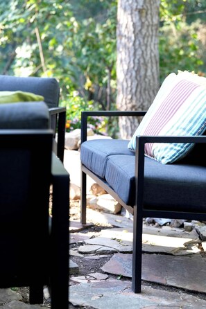 A stone patio with a black metal chair and a cushioned bench with a striped pillow.