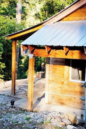 A wooden cabin with a metal roof, surrounded by a stone pathway and gravel, set in a forested area. - Cozy Nature Retreat Cabin with Fireplace (Midway)