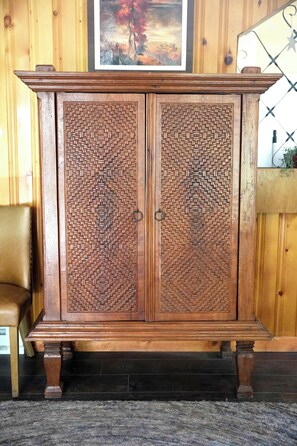 A wooden cabinet with intricate carvings, a cushioned chair, and a framed picture on the wall.