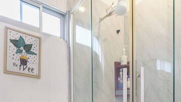 A modern bathroom with a glass-enclosed shower, a wooden bench, and a potted plant with the text "Be Free".