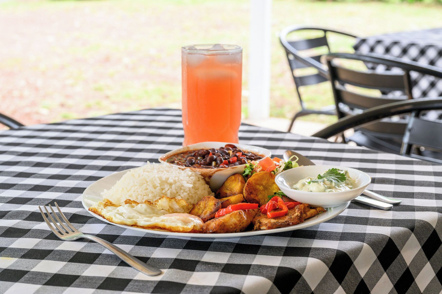 A meal with rice, beans, fried plantains, and a salad on a checkered tablecloth.