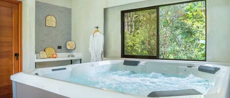 Habitación de spa con bañera de hidromasaje, puerta de madera, ventana con vistas a árboles y una placa en la pared.