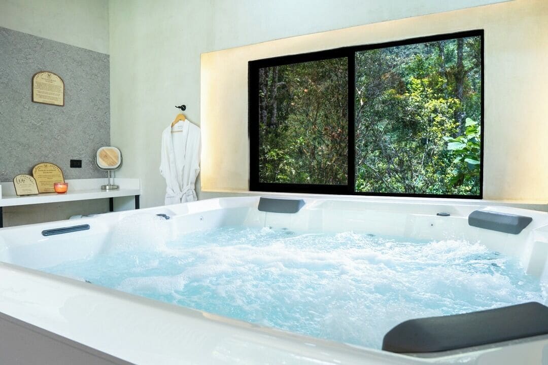 Un baño moderno con una bañera grande, un tocador con espejo y una ventana con vistas a la vegetación.