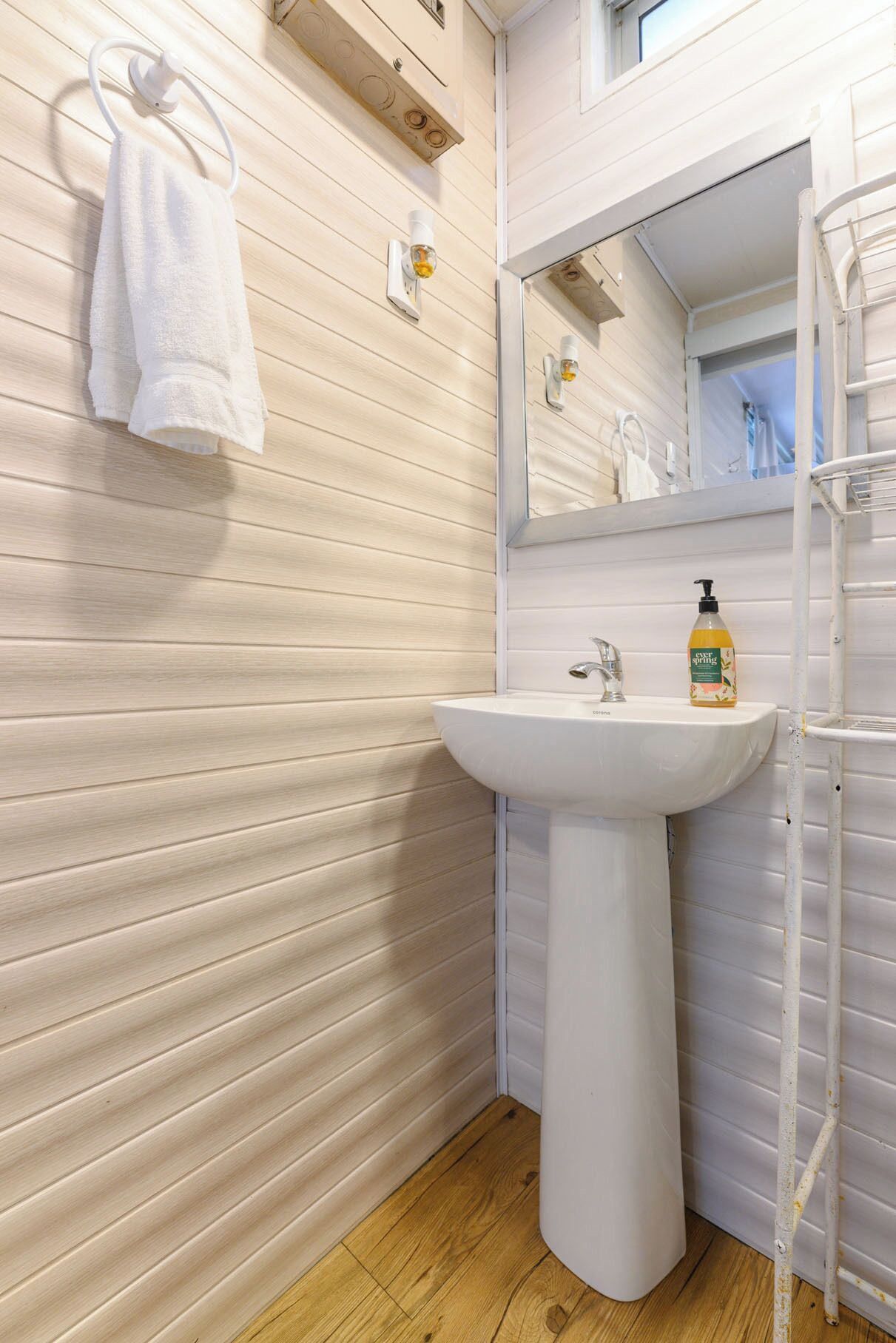 Un baño con un lavamanos blanco, un espejo y un perchero para toallas.