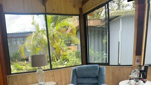 Ein Zimmer mit blauem Ohrensessel, einem kleinen runden Tisch mit Lampe und einem weißen Tisch mit Kaffeemaschine.