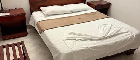 A neatly made bed with white bedding, a wooden headboard, and a bedside table with a lamp.