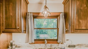 Une cuisine avec des meubles en bois, un plan de travail en marbre, un évier en acier inoxydable et une fenêtre avec des rideaux.