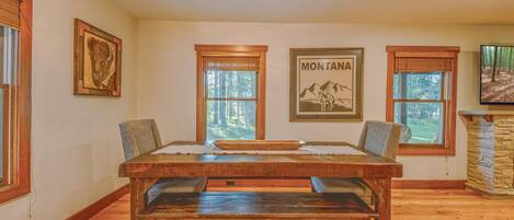 Un comedor con una mesa de madera, bancos, cuadros enmarcados y ventanas que dan a vistas de árboles.