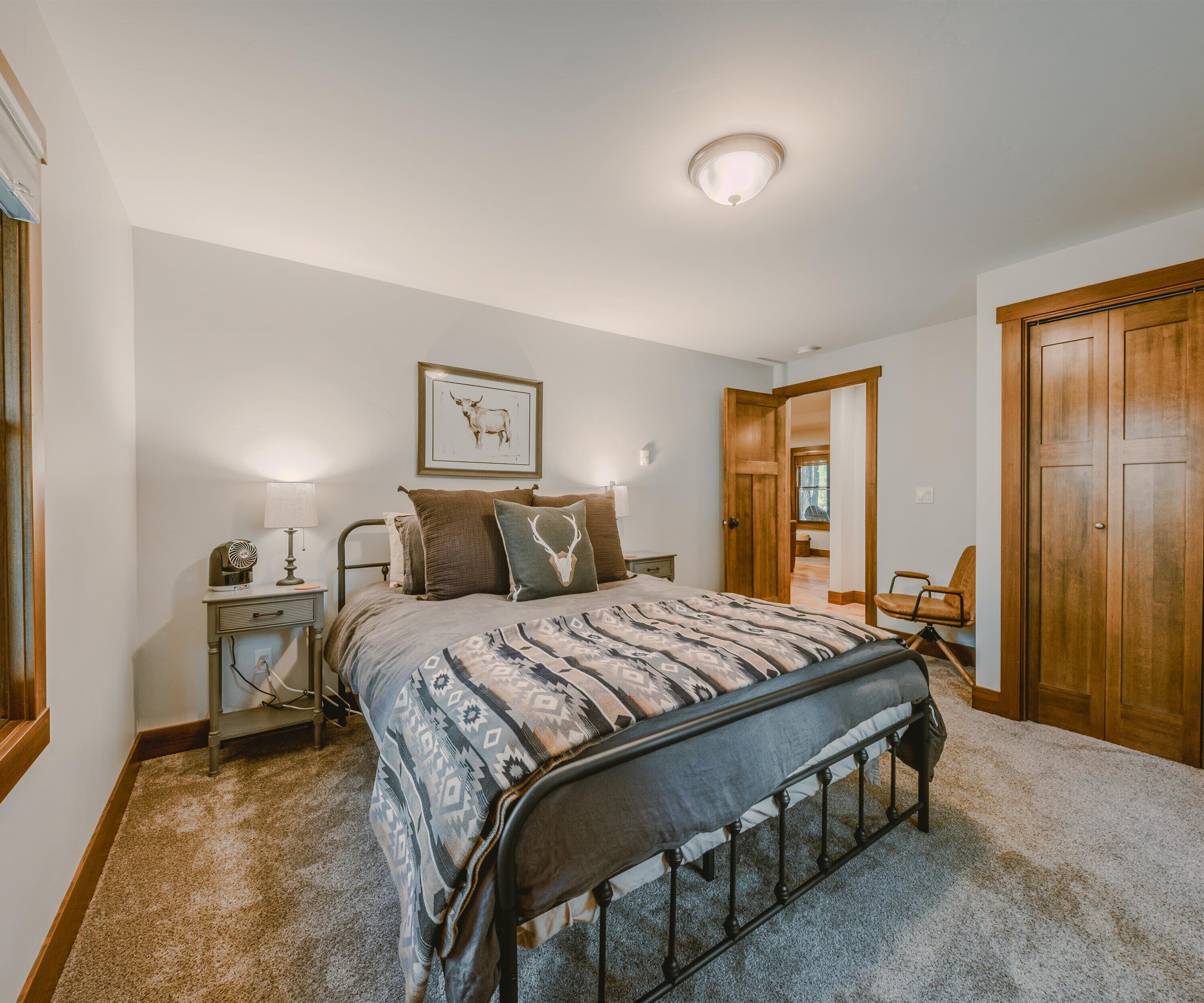 A bedroom with a bed, bedside tables, a lamp, a framed picture on the wall, and a wooden door.