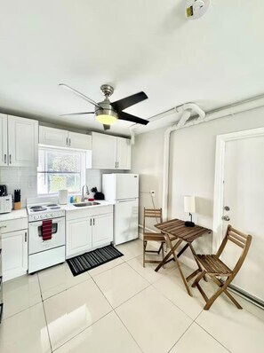 A compact kitchen with white cabinets, a stove, a refrigerator, and a dining area with a table and chairs.