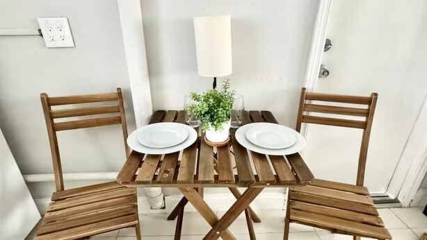A wooden dining table with four chairs, a small potted plant, and a white lamp on a white tiled floor.
