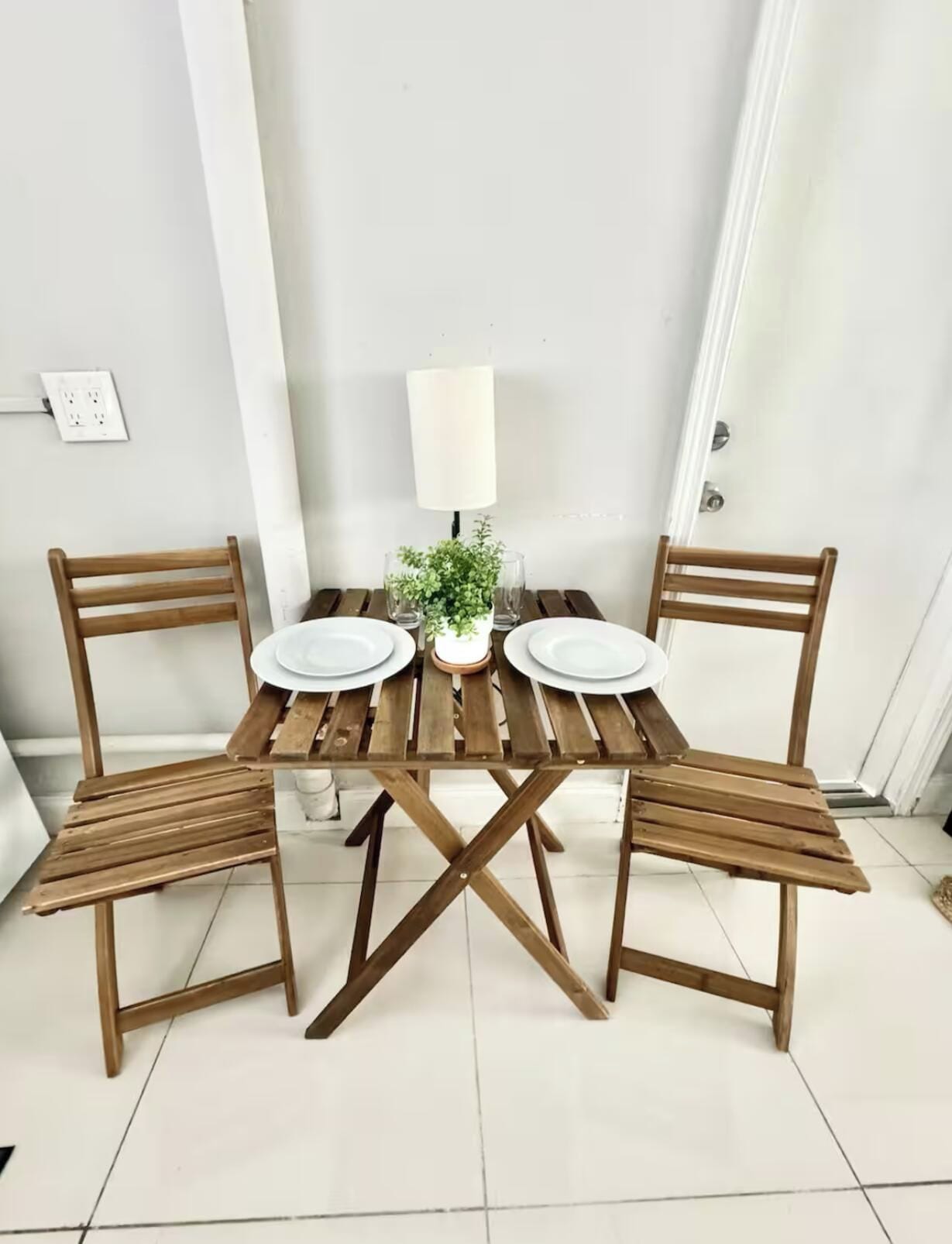 Una mesa de madera para comer con dos sillas, una planta pequeña en maceta y una lámpara de mesa.