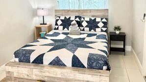 A bedroom with a bed, a ceiling fan, a nightstand, a lamp, and a small plant.