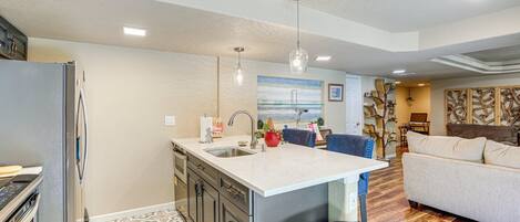Una cocina moderna con una isla central, electrodomésticos de acero inoxidable y una zona de comedor con sofá y mesa de centro.