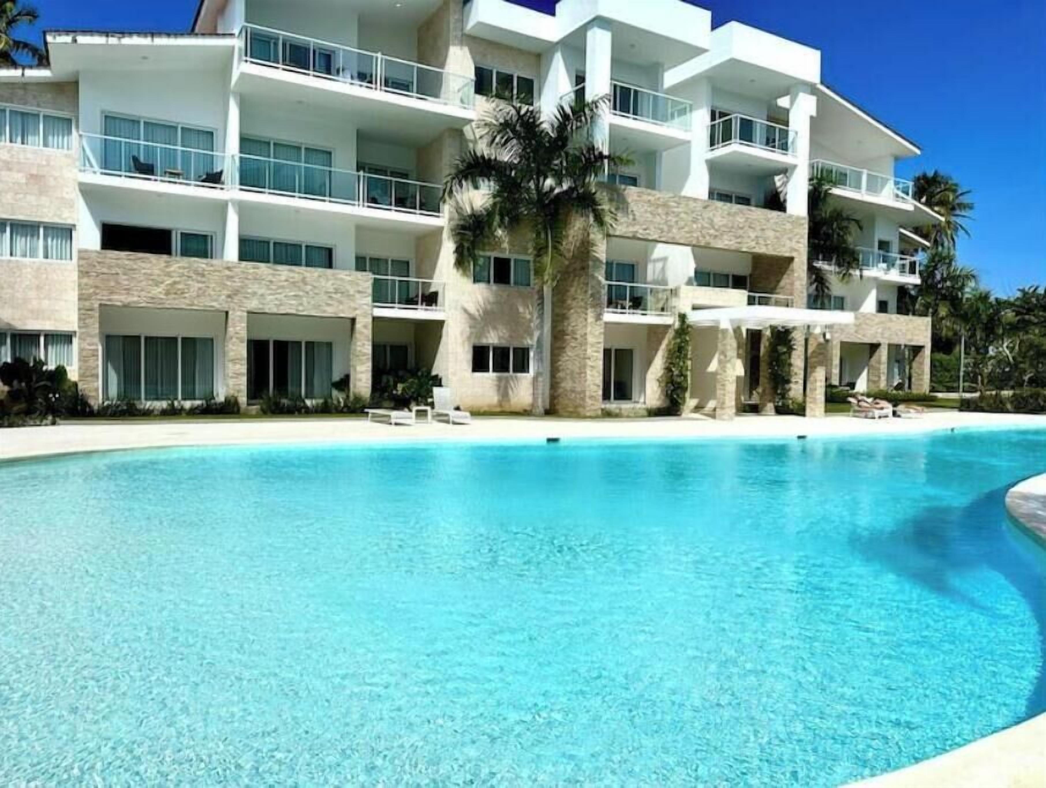 Un hôtel à plusieurs étages doté d’une piscine, de palmiers et surplombant un ciel d’un bleu limpide.