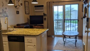 A kitchen with a dishwasher, a dining area with a table, a TV, and a sliding glass door leading to an outdoor patio. - C&D REST-A-WHILE Book 2 Nights 3rd Is Free 9-1-26 to 9-27-26 Stays Only (Oak Harbor)