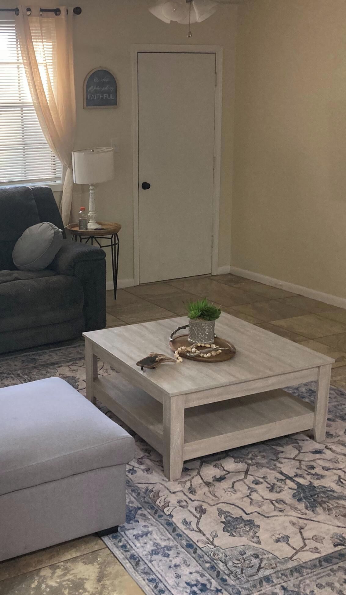 Un salon avec un canapé de couleur claire, une petite table ronde avec une lampe, une table basse agrémentée d’objets décoratifs et un tapis à motifs.