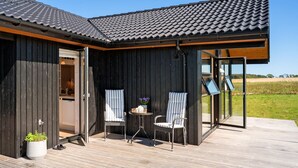 Une maison moderne dotée d’une terrasse en bois, de deux chaises, d’une petite table et d’une plante en pot.