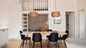 Un espace repas avec une table en bois, des chaises noires et une chambre à l’étage avec une fenêtre.
