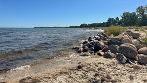 Une côte rocheuse bordée d’une eau claire, avec une ligne d’arbres visible au loin.
