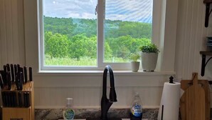 A kitchen with a white sink, a window with a view of greenery, and a knife block on the counter. - Farmhouse & Rustic Patio with Beautiful Views! (Saint Joe)