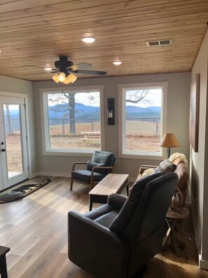 A room with a ceiling fan, large windows with a view of mountains, a sofa, and a small table. - Farmhouse & Rustic Patio with Beautiful Views! (Saint Joe)