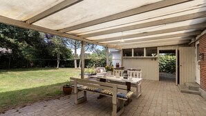 Un patio cubierto con mesa, sillas, un banco y una planta en maceta.