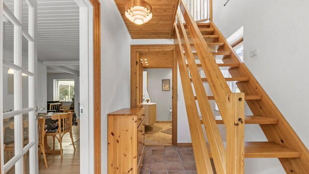 Una escalera de madera conduce a un nivel superior, con una zona de cocina, una mesa de comedor y un baño que incluye inodoro y lavamanos.